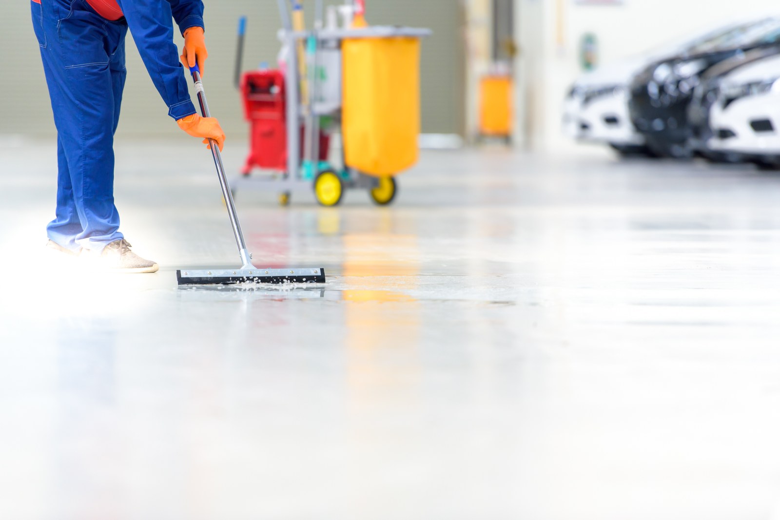 Worker using a squeegee mop to clean a glossy epoxy-coated garage floor