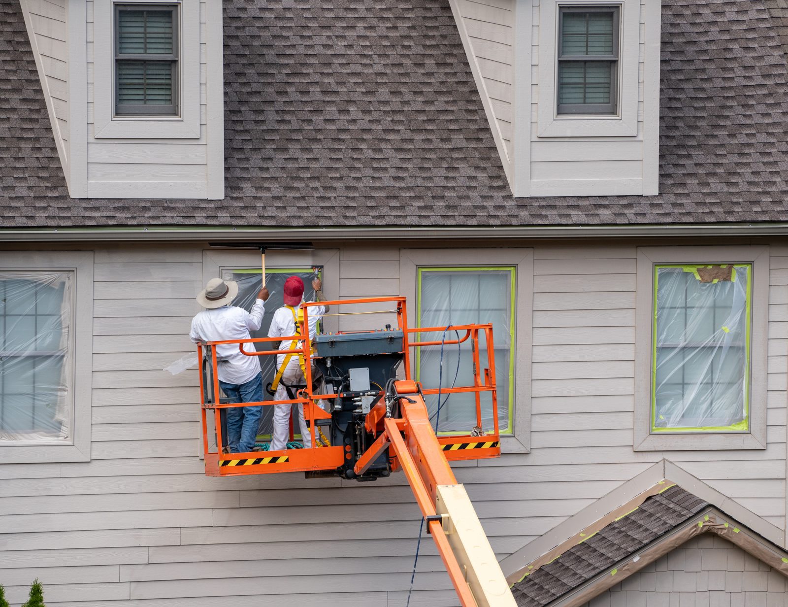 Two professional painters on an articulating lift painting the exterior of a home