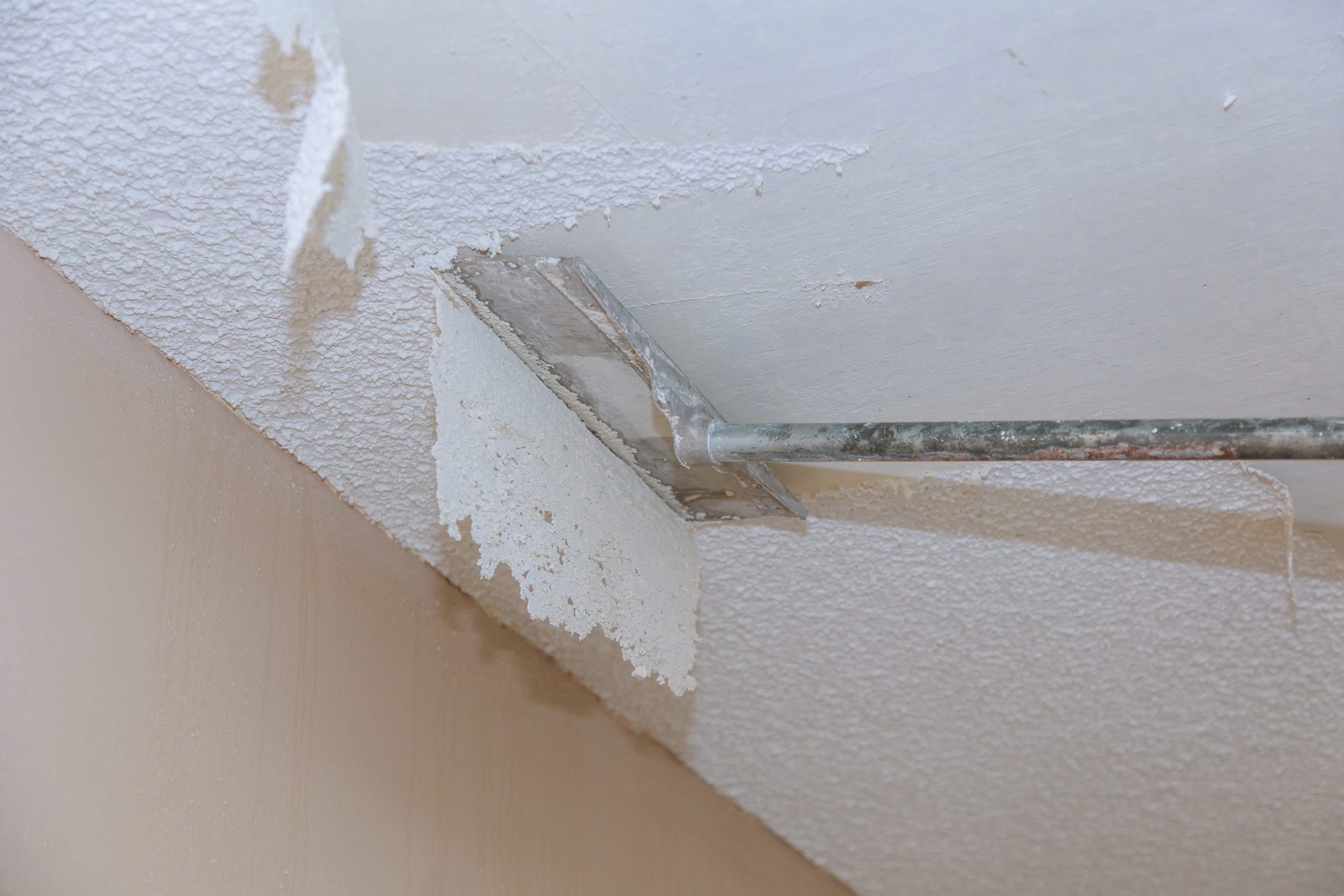 A putty knife scraping textured popcorn ceiling off during a home renovation